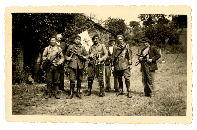 Résistants du maquis posant avec leurs armes et un drapeau devant une ferme