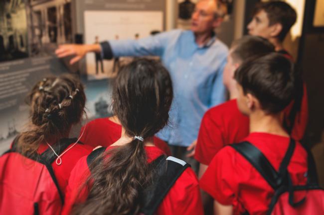 Groupe d’élèves écoutant les explications d’un médiateur devant un panneau d’exposition