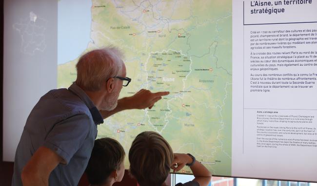 Visiteurs observant un panneau cartographique présentant l’Aisne comme territoire stratégique au Musée de la Résistance et de la Déportation de l’Aisne