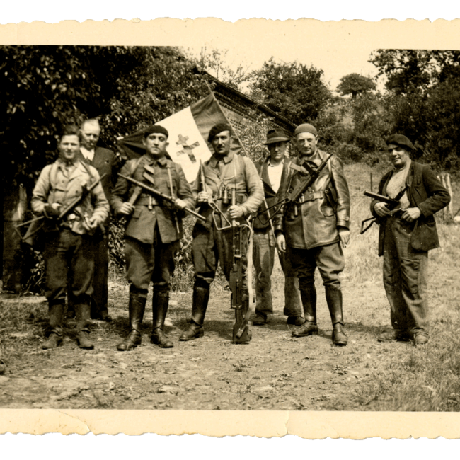 Résistants du maquis posant avec leurs armes et un drapeau devant une ferme