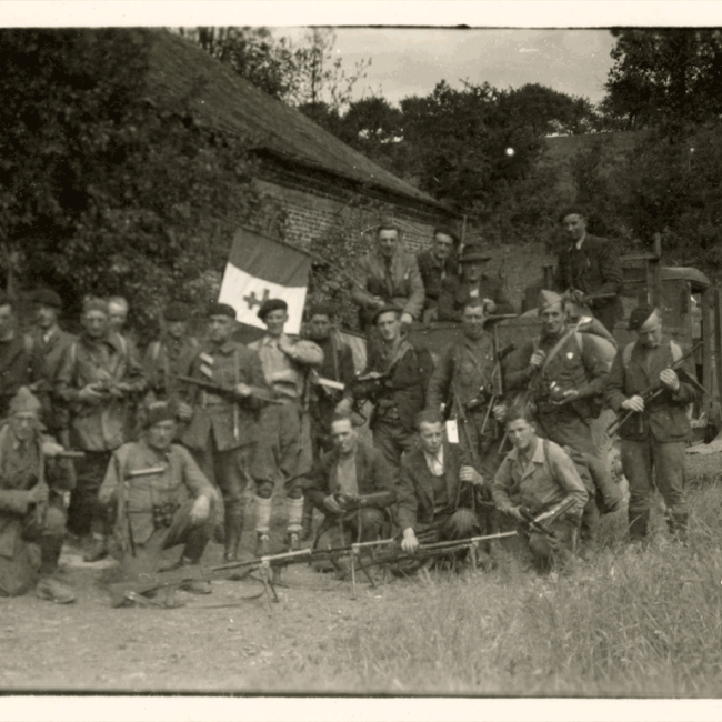 Groupe de résistants du maquis rassemblés avec armes et drapeau devant une ferme