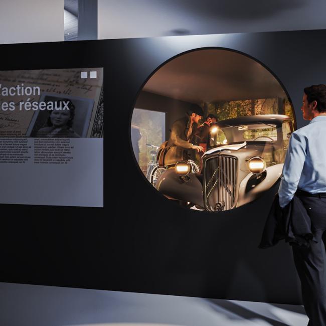 Visiteur devant un diorama montrant une scène de Résistance autour d’une voiture 